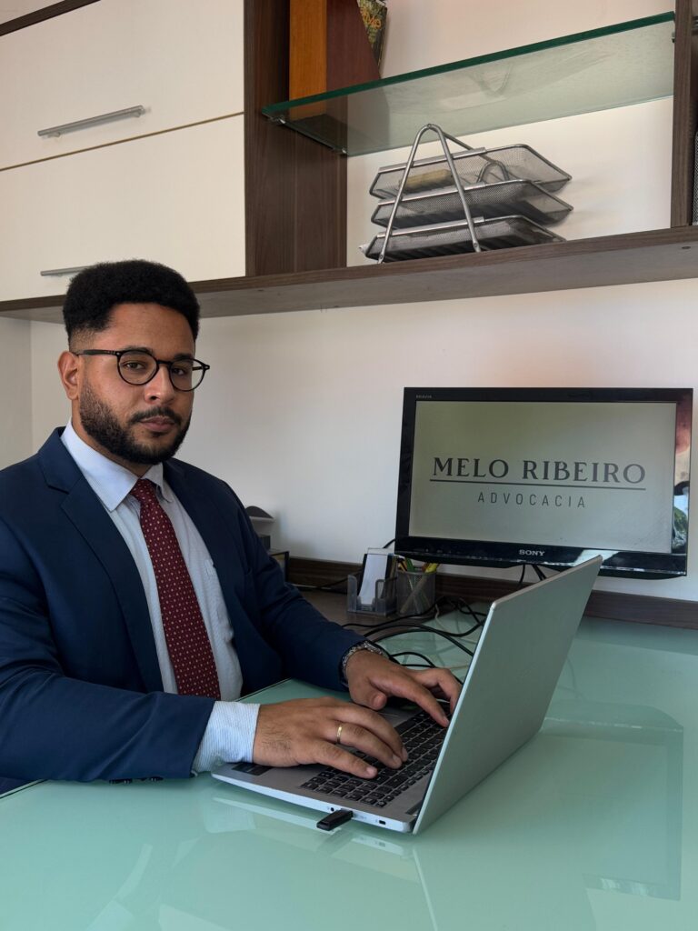 Foto do sócio fundador, Nelson Melo Ribeiro, no escritório utilizando o notebook e com a logomarca do escritório na segunda tela.